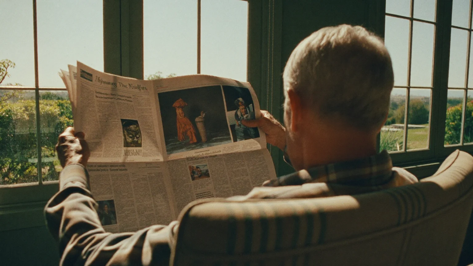 Older man reading a newspaper in a sunlit armchair by a window