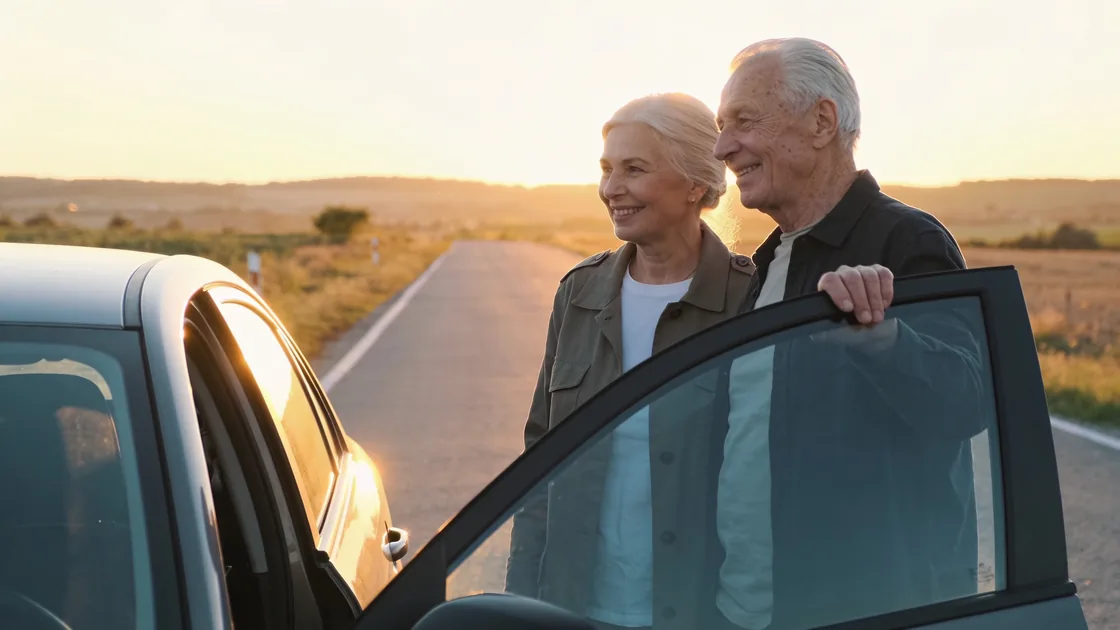 Older couple beside their car on a country road at golden hour