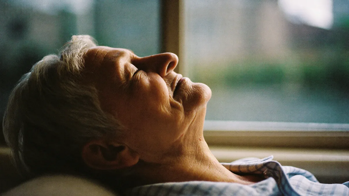 Older adult resting by a window in soft evening light with eyes closed, away from screens