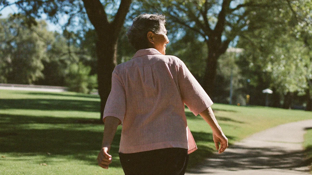Older woman walking outdoors on a sunlit park path