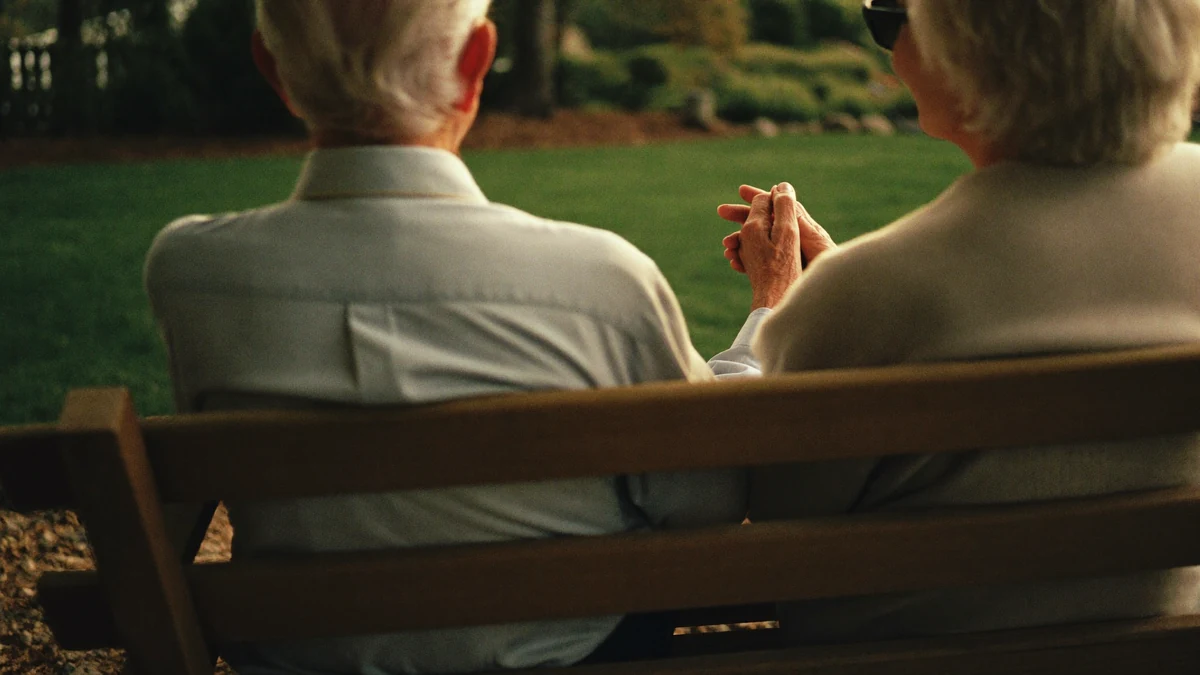 Elderly couple sitting close together on a garden bench in golden evening light